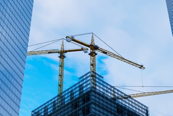 Tower cranes beside a glass office building under construction