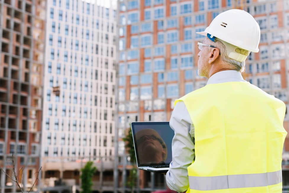 Site engineer reviewing plans in front of a residential tower under construction